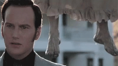 A Man In A Suit Is Standing Next To A Statue Of A Woman Hanging From A Building . GIF