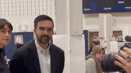 A Man In A Suit Is Standing Next To A Woman In A Hijab While Being Photographed By A Camera . GIF