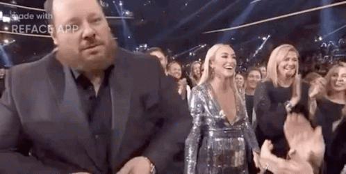 A Man In A Suit Is Standing Next To A Woman In A Sequined Dress . GIF