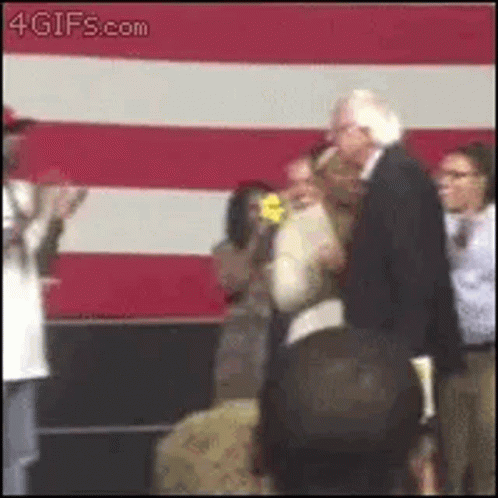 A Man In A Suit Is Standing Next To A Woman In Front Of A Red And White Striped Wall . GIF