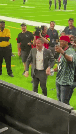 A Man In A Suit Is Standing On A Football Field Surrounded By People GIF