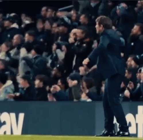 A Man In A Suit Is Standing On A Soccer Field In Front Of A Crowd Of People . GIF