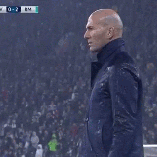 A Man In A Suit Is Standing On A Soccer Field With His Hand On His Forehead . GIF