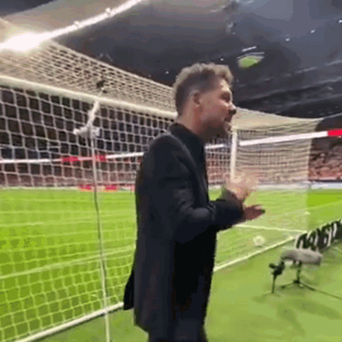A Man In A Suit Is Standing On A Soccer Field With His Hands Outstretched . GIF