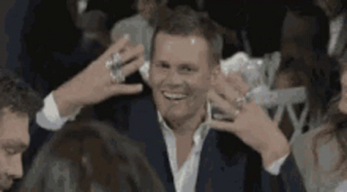 A Man In A Suit Is Surrounded By People While Holding A Drink . GIF