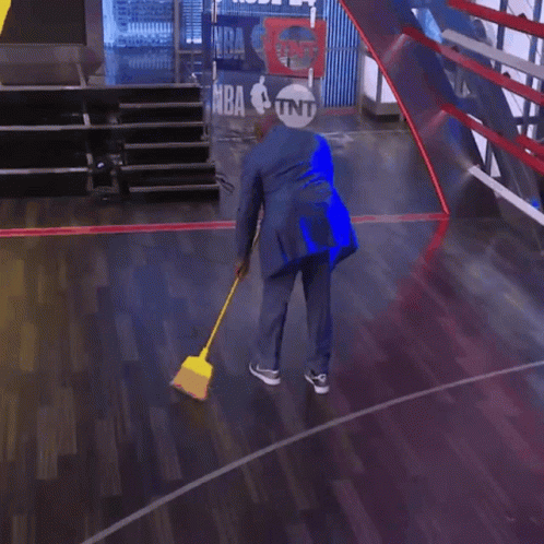 A Man In A Suit Is Sweeping The Floor In Front Of A Sign That Says Nba On It GIF