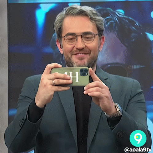 A Man In A Suit Is Taking A Picture Of Himself With A Phone With The Letter H On It GIF