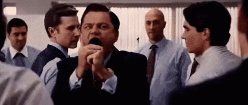 A Man In A Suit Is Talking Into A Microphone While Standing In A Crowd Of People . GIF