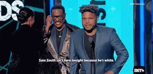 A Man In A Suit Is Talking Into A Microphone While Standing Next To Another Man . GIF