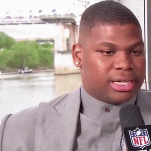 A Man In A Suit Is Talking Into A Microphone With The Nfl Logo On It GIF