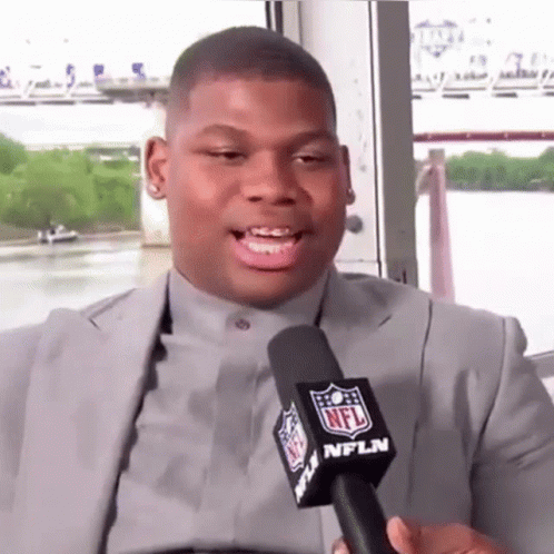 A Man In A Suit Is Talking Into An Nfl Microphone . GIF