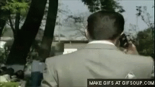 A Man In A Suit Is Talking On A Cell Phone In The Park . GIF