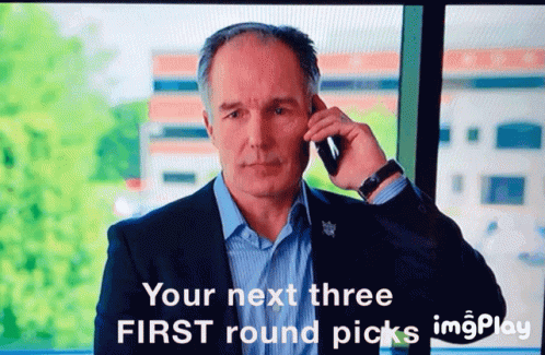 A Man In A Suit Is Talking On A Cell Phone With The Words " Your Next Three First Round Picks " Above Him GIF