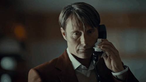A Man In A Suit Is Talking On A Phone And Wiping His Face With A Napkin GIF
