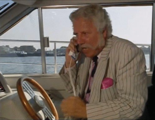 A Man In A Suit Is Talking On A Phone While Driving A Boat GIF