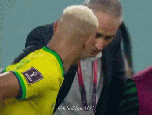 a man in a suit is talking to a soccer player who is wearing a yellow shirt with the number 1 on it .