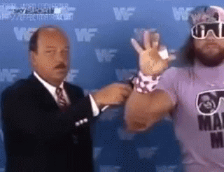 A Man In A Suit Is Talking To A Wrestler In A Purple Shirt . GIF