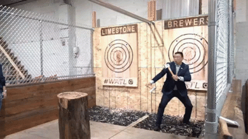 A Man In A Suit Is Throwing An Axe At A Target That Says Limestone Brewers On It GIF