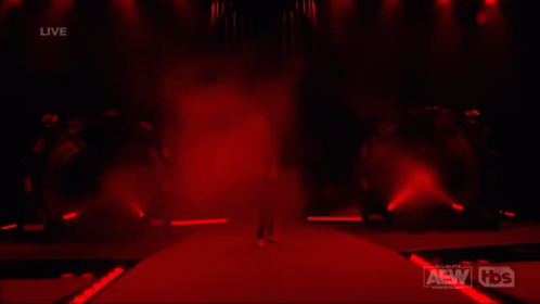 A Man In A Suit Is Walking Down A Red Carpet In Front Of A Live Aew Wrestling Event GIF