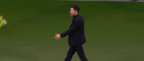 A Man In A Suit Is Walking On A Soccer Field While A Person Throws A Yellow Shoe . GIF