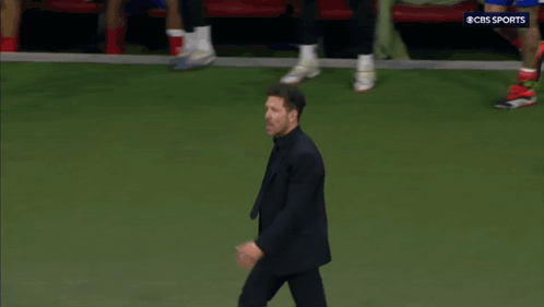 A Man In A Suit Is Walking On A Soccer Field With A Cbs Sports Logo In The Background GIF