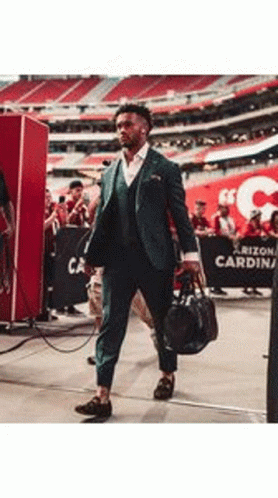 A Man In A Suit Is Walking Through A Stadium Holding A Bag . GIF