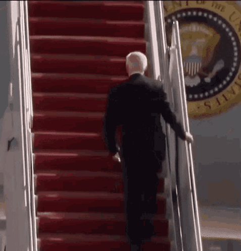 A Man In A Suit Is Walking Up The Stairs Of A Plane . GIF
