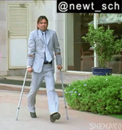 A Man In A Suit Is Walking With Crutches In Front Of A Building GIF