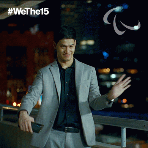 A Man In A Suit Is Waving His Hand In Front Of A Sign That Says #Wethel5 GIF