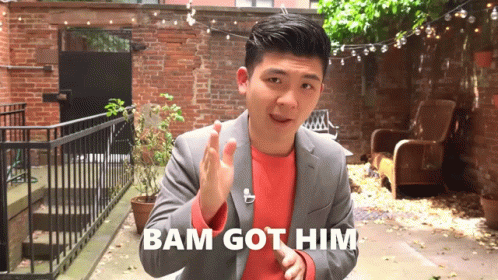 A Man In A Suit Says Bam Got Him While Standing In Front Of A Brick Wall GIF