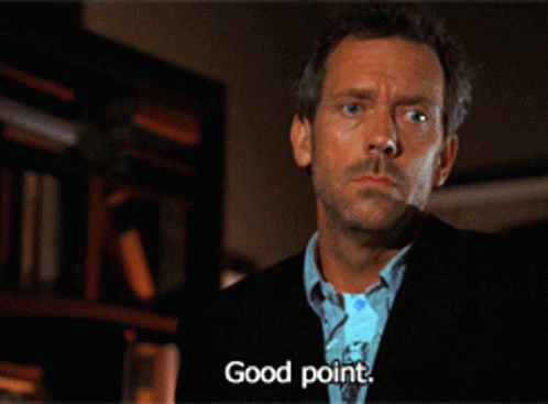 A Man In A Suit Says " Good Point " In Front Of A Bookshelf GIF