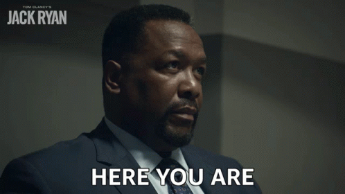 A Man In A Suit Says Here You Are In Front Of A Poster For Tom Clancy 'S Jack Ryan GIF