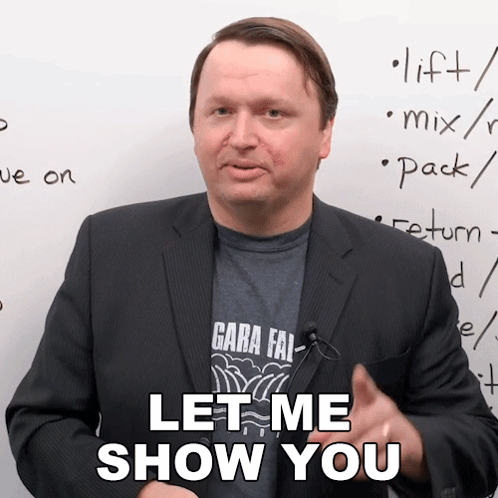 A Man In A Suit Says " Let Me Show You " In Front Of A White Board GIF