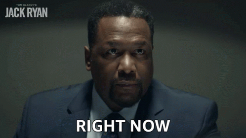 A Man In A Suit Says Right Now In Front Of A Poster For Jack Ryan GIF