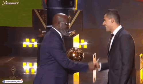 A Man In A Suit Shakes Hands With A Man In A Tuxedo GIF