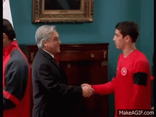 A Man In A Suit Shaking Hands With A Man In A Red Shirt GIF