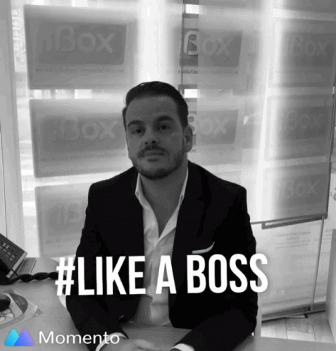 A Man In A Suit Sits At A Desk In Front Of A Window That Says Box On It GIF