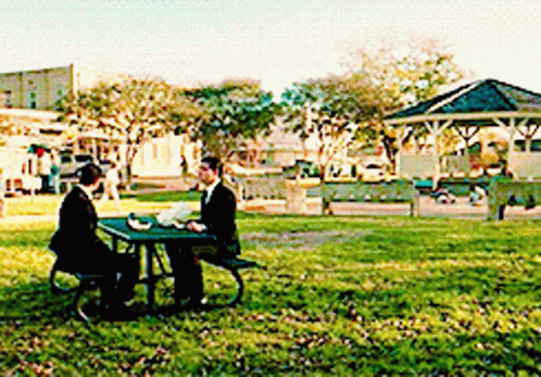 a man in a suit sits at a picnic table in a park