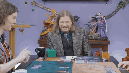 A Man In A Suit Sits At A Table Playing A Game Of Cards GIF