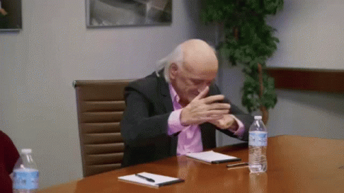 A Man In A Suit Sits At A Table With A Bottle Of Aquafina Water GIF
