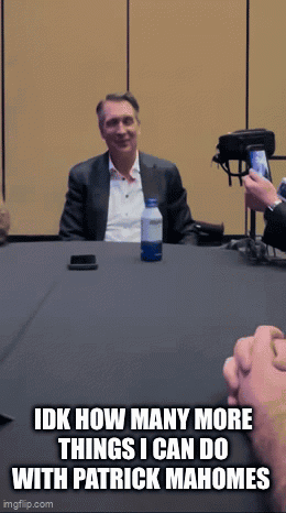 A Man In A Suit Sits At A Table With A Bottle Of Water And A Cell Phone GIF