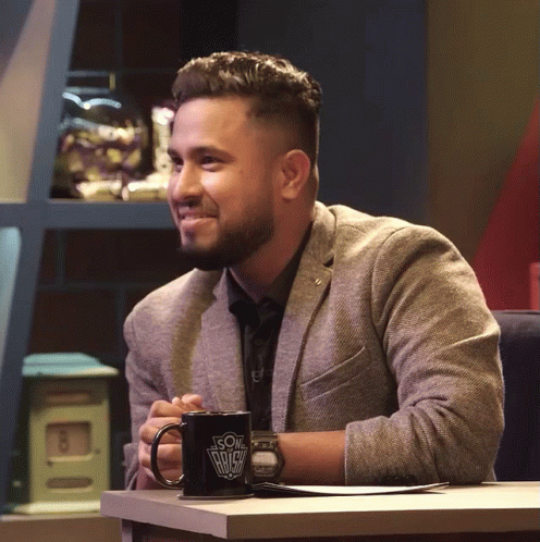 A Man In A Suit Sits At A Table With A Coffee Mug That Says ' Son Of A Bitch ' On It GIF