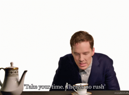 A Man In A Suit Sits At A Table With A Cup Of Tea And Says Take Your Time There 'S No Rush ' GIF
