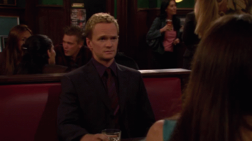 A Man In A Suit Sits At A Table With A Glass Of Whiskey And A Bowl Of Food GIF