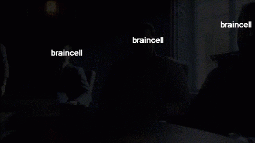A Man In A Suit Sits At A Table With The Words Braincell On His Face GIF