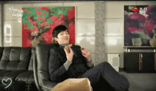 A Man In A Suit Sits In A Chair Eating A Burger GIF