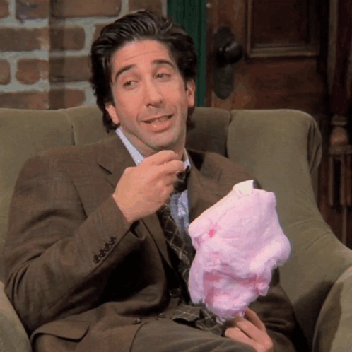 A Man In A Suit Sits In A Chair Eating Cotton Candy GIF