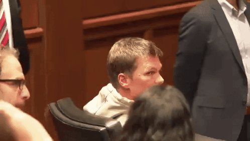 A Man In A Suit Sits In A Chair With A Woman Behind Him GIF
