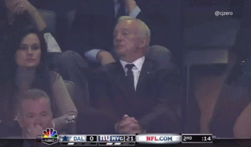A Man In A Suit Sits In A Stadium Watching A Game Between Dallas And New York Giants GIF