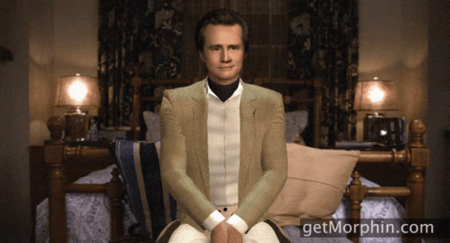 A Man In A Suit Sits In Front Of A Bed With The Website Getmorphin.com GIF